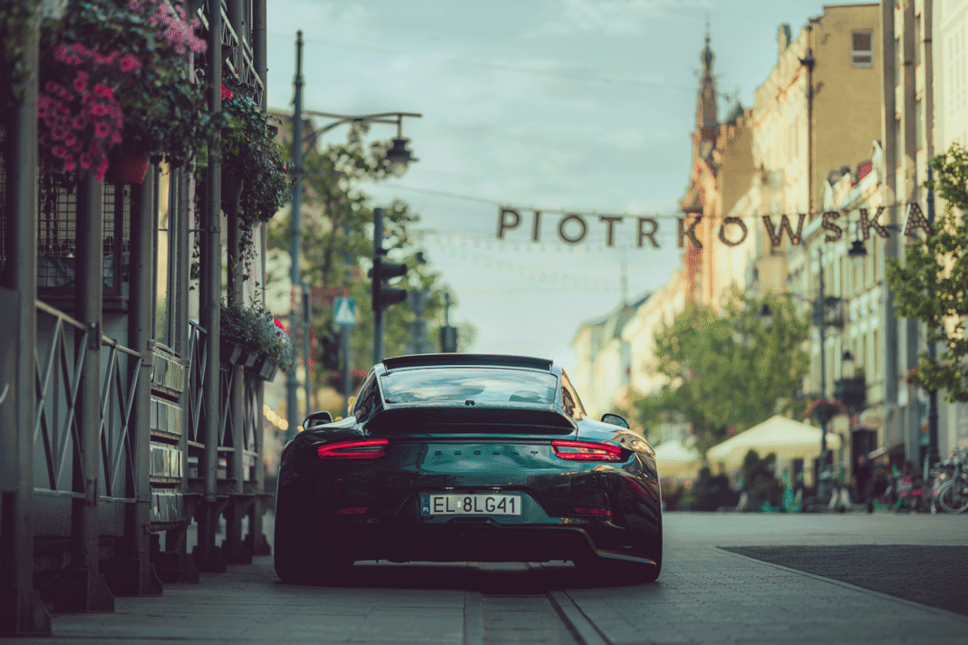 The Indecent 007, a custom dark green Porsche 911 with widebody styling and a ducktail spoiler, is parked on Piotrkowska Street in Łódź, Poland. The rear view shows the 